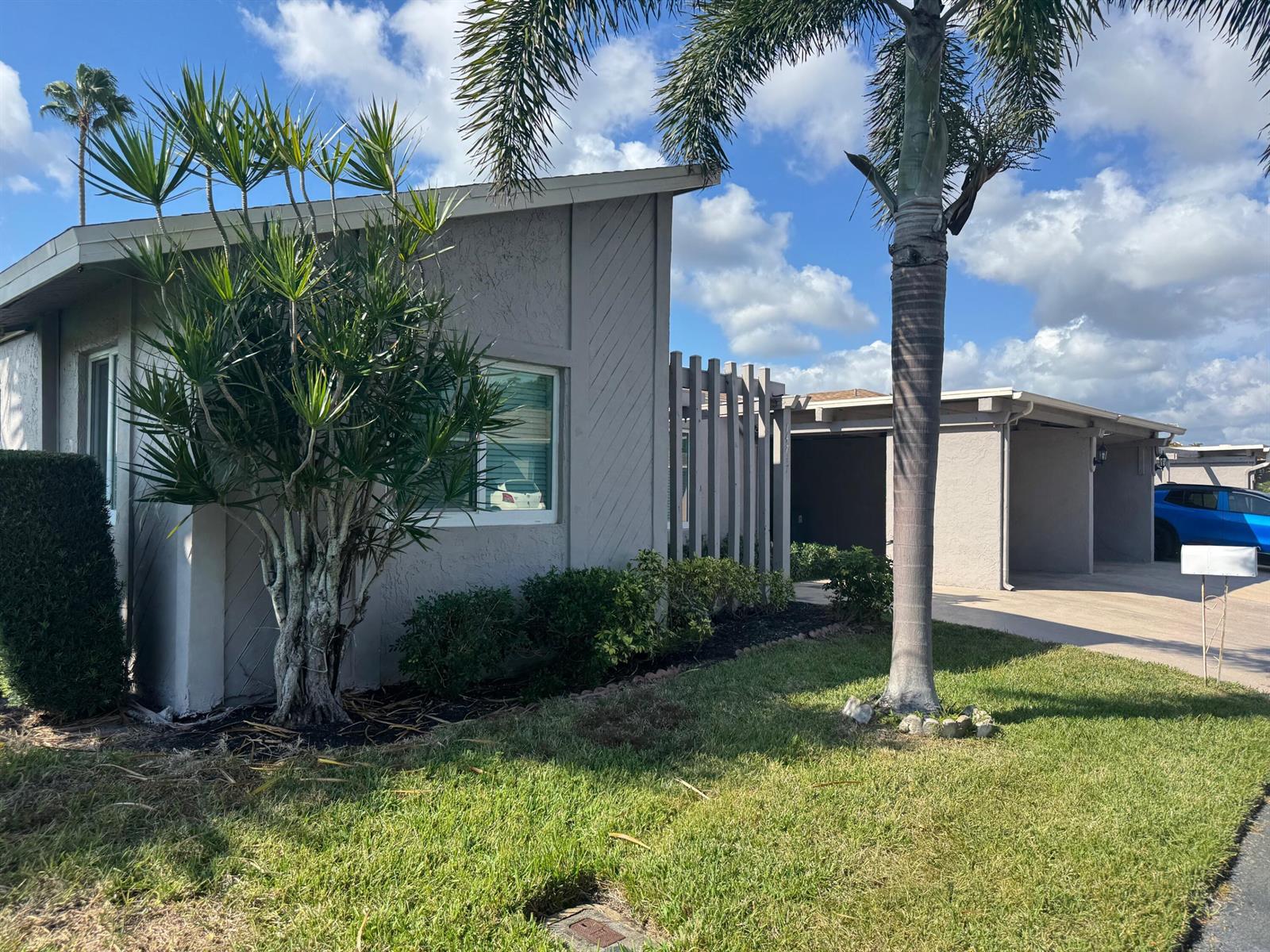 A single-story house with gray siding, a palm tree, and a carport under a blue sky — 14747 Wildflower Lane, Delray Beach FL 33446, DELRAY BEACH, FL