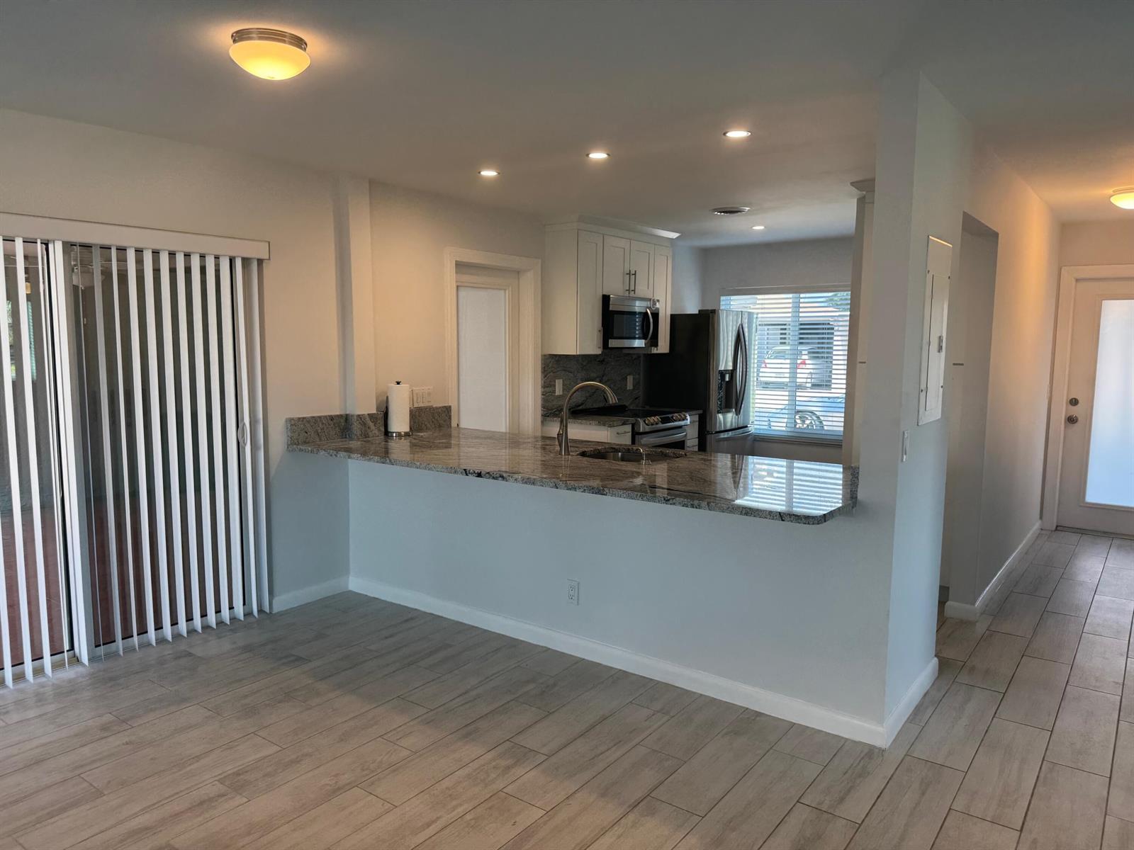 A kitchen features granite countertops, white cabinets, stainless steel appliances, and light wood-look tile flooring — 14747 Wildflower Lane, Delray Beach FL 33446, DELRAY BEACH, FL