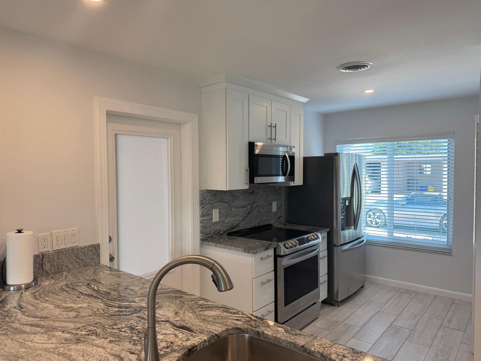 A kitchen features white cabinets, granite countertops, stainless steel appliances, and a window with blinds — 14747 Wildflower Lane, Delray Beach FL 33446, DELRAY BEACH, FL
