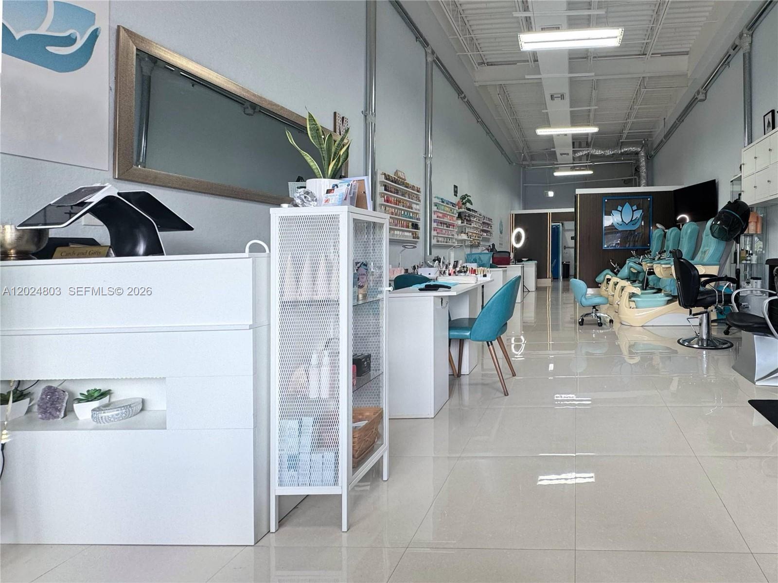 A bright nail salon features white workstations, teal chairs, and a polished tile floor — TAMARAC, FL