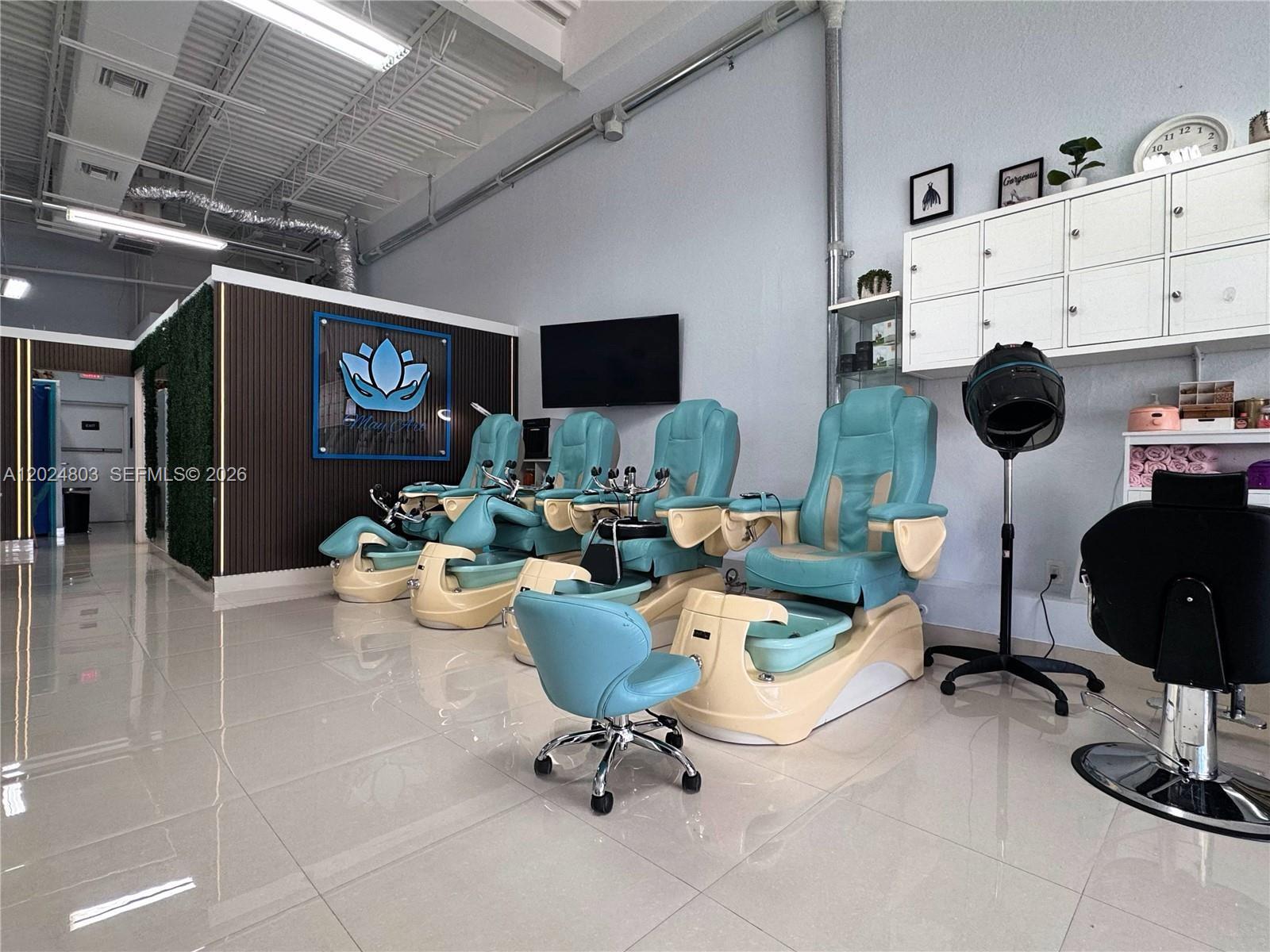 A salon interior features four teal pedicure chairs, a rolling stool, and white storage cabinets — TAMARAC, FL
