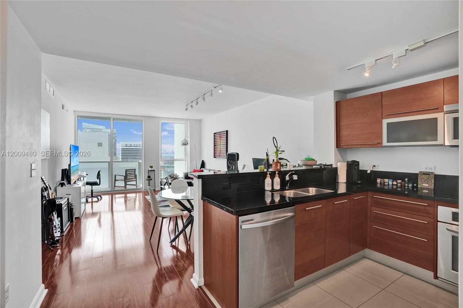 A kitchen with dark wood cabinets and black countertops opens into a living area — 253 NE 2nd St # 3304, Miami FL 33132, MIAMI, FL