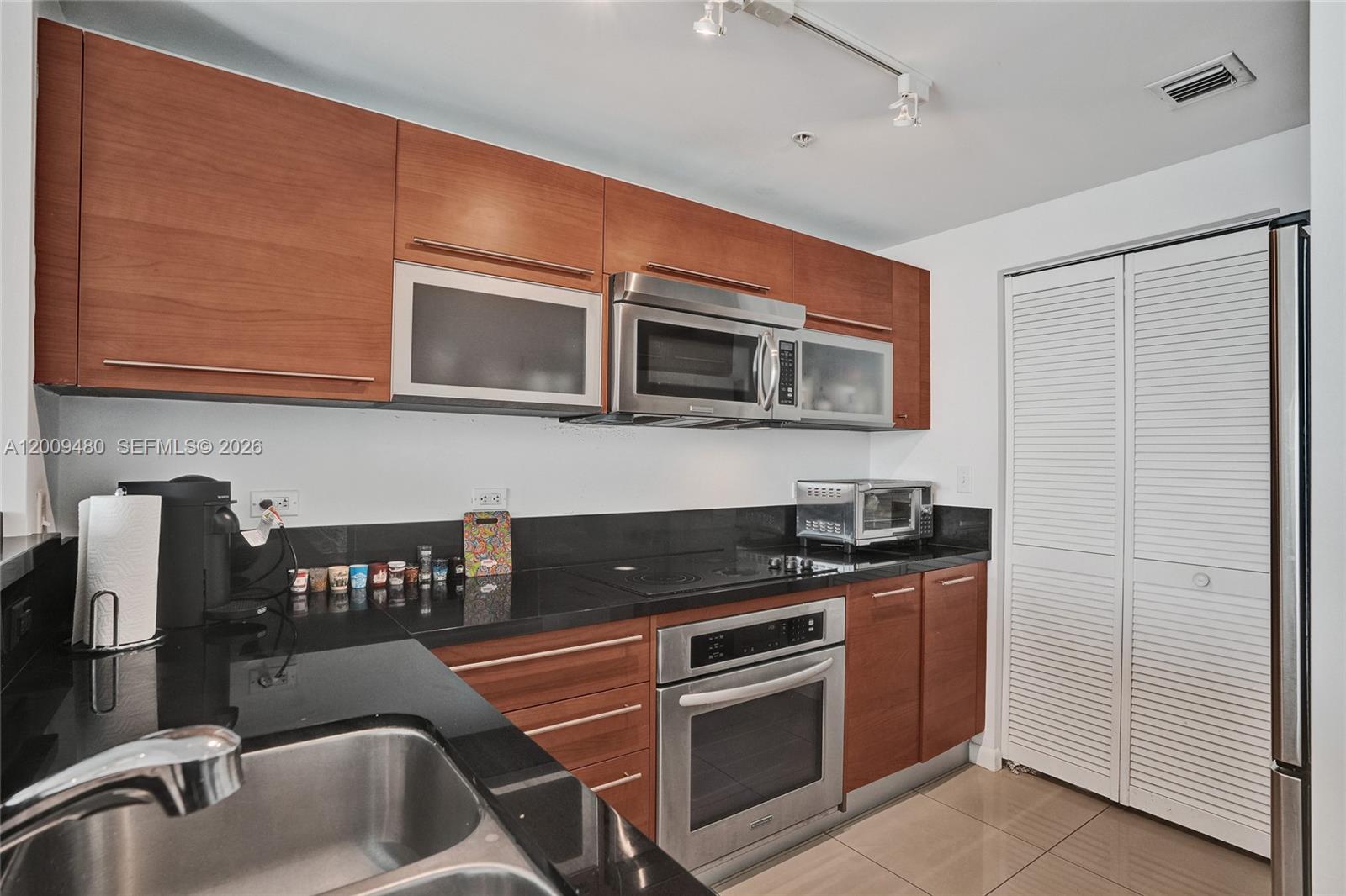 A kitchen features wood cabinets, black countertops, stainless steel appliances, and white louvered closet doors — 253 NE 2nd St # 3304, Miami FL 33132, MIAMI, FL