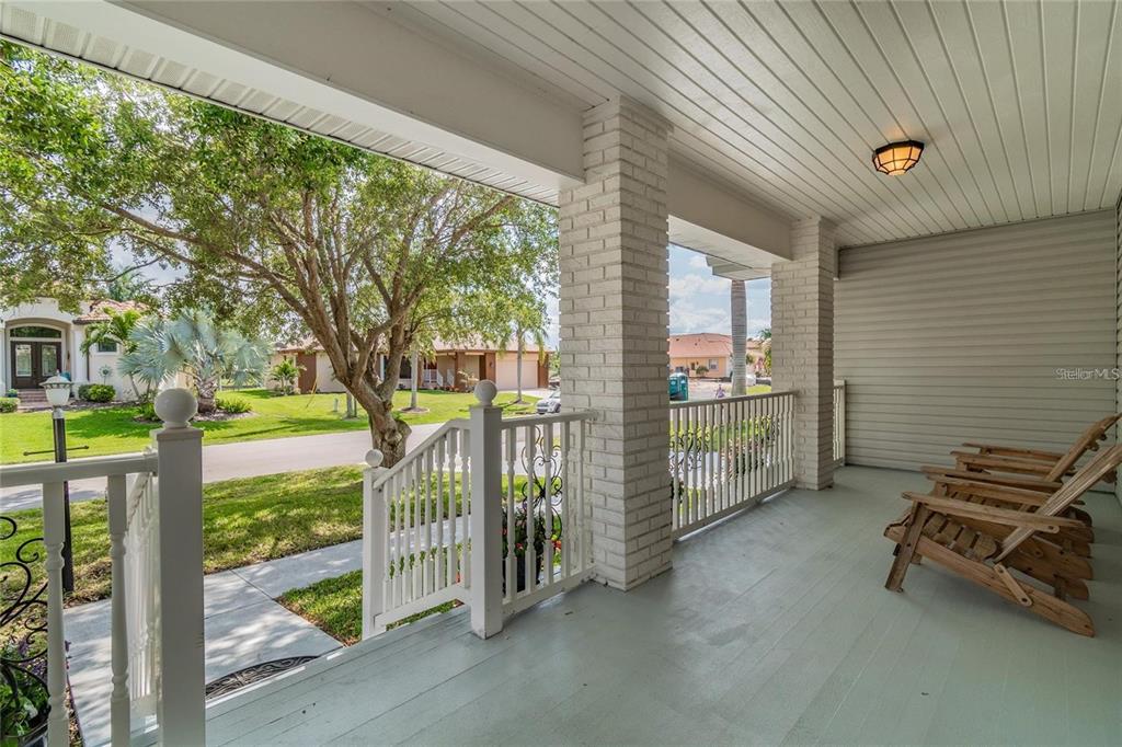 A covered porch features white railings, brick columns, and wooden chairs overlooking a suburban street — 340 PORTOFINO DRIVE, PUNTA GORDA, FL