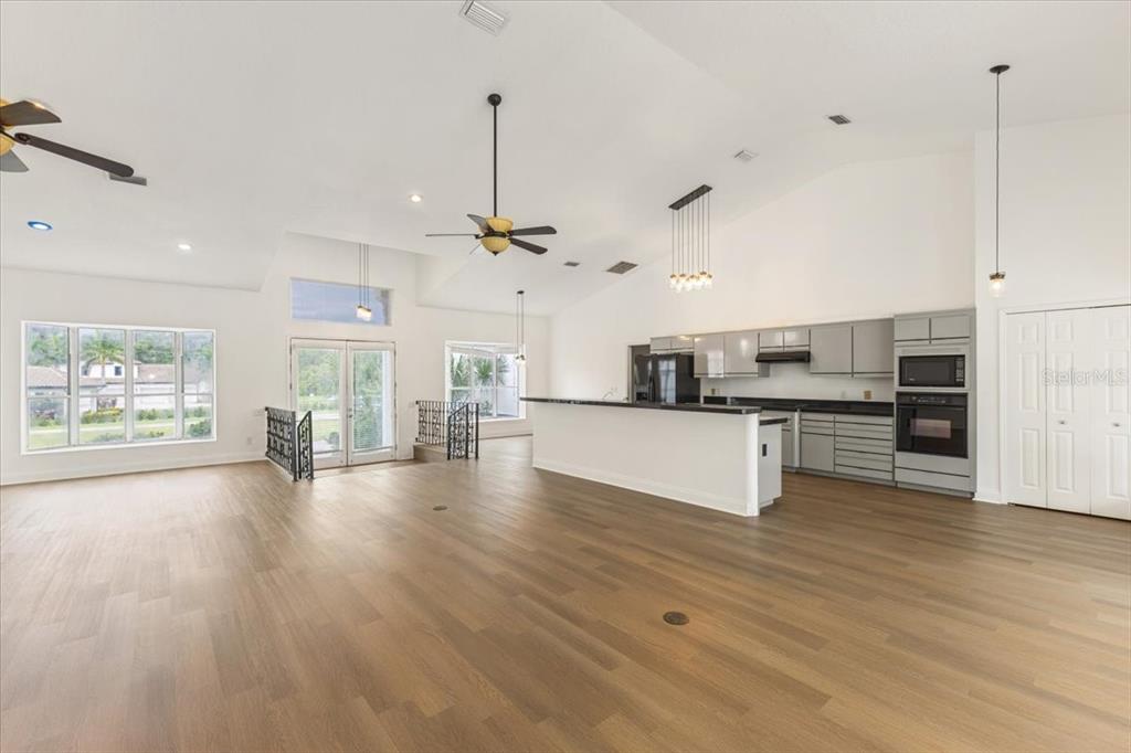 An open-concept living area features light wood flooring, a kitchen with gray cabinets, and vaulted ceilings — 12001 LAKE BUTLER BOULEVARD, WINDERMERE, FL
