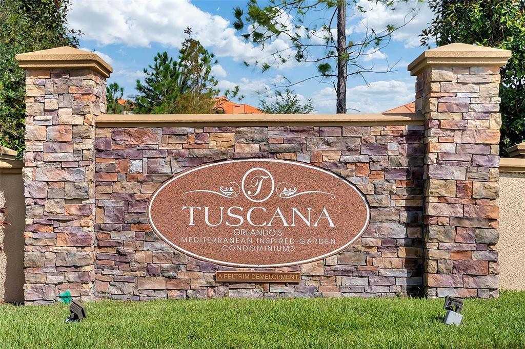A stone monument sign for Tuscana condominiums stands in a grassy area under a blue sky — 1371 TUSCAN TER UNIT 3307, DAVENPORT, FL