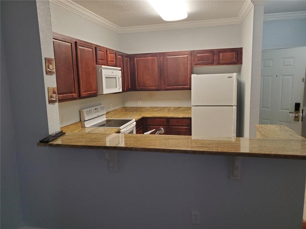 A kitchen features dark wood cabinets, granite countertops, and white appliances — 1371 TUSCAN TER UNIT 3307, DAVENPORT, FL
