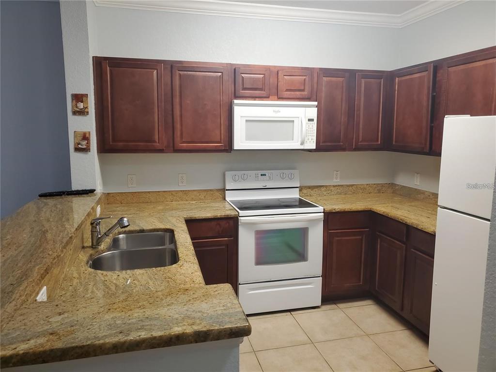 A kitchen features dark wood cabinets, granite countertops, white appliances, and light-colored tile flooring — 1371 TUSCAN TER UNIT 3307, DAVENPORT, FL