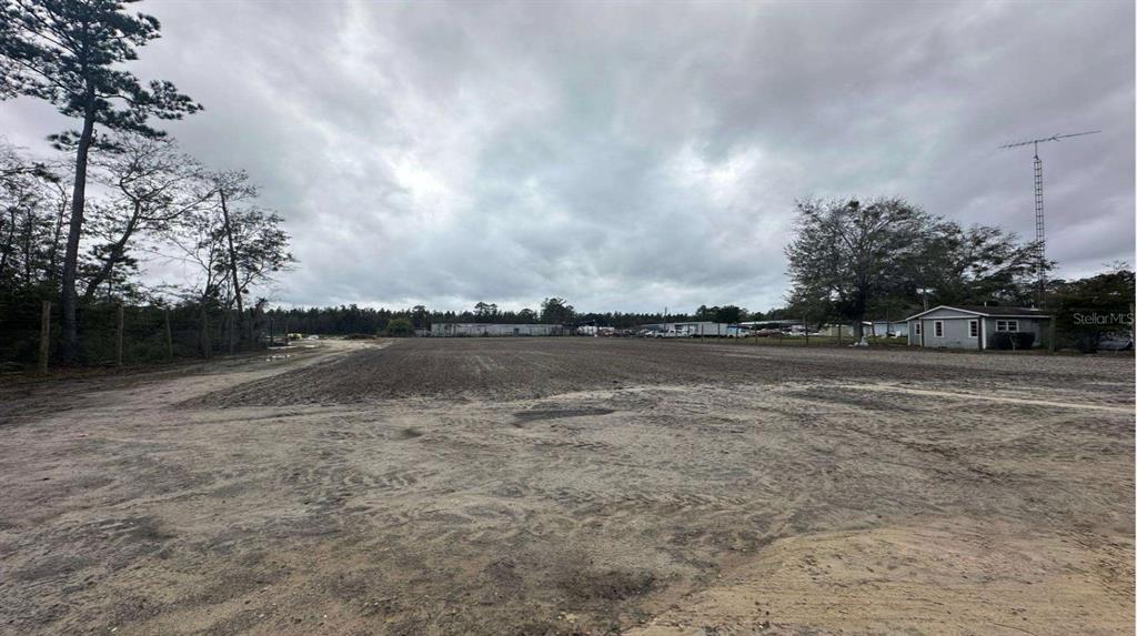 A large, cleared, sandy lot under a cloudy sky with trees and a small house — 20065 SE HAWTHORNE ROAD, HAWTHORNE, FL