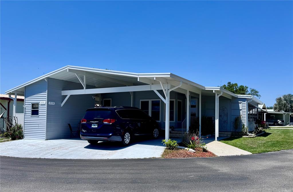A light blue manufactured home features a carport with a dark blue minivan parked underneath — 2055 S FLORAL AVENUE UNIT 230, BARTOW, FL