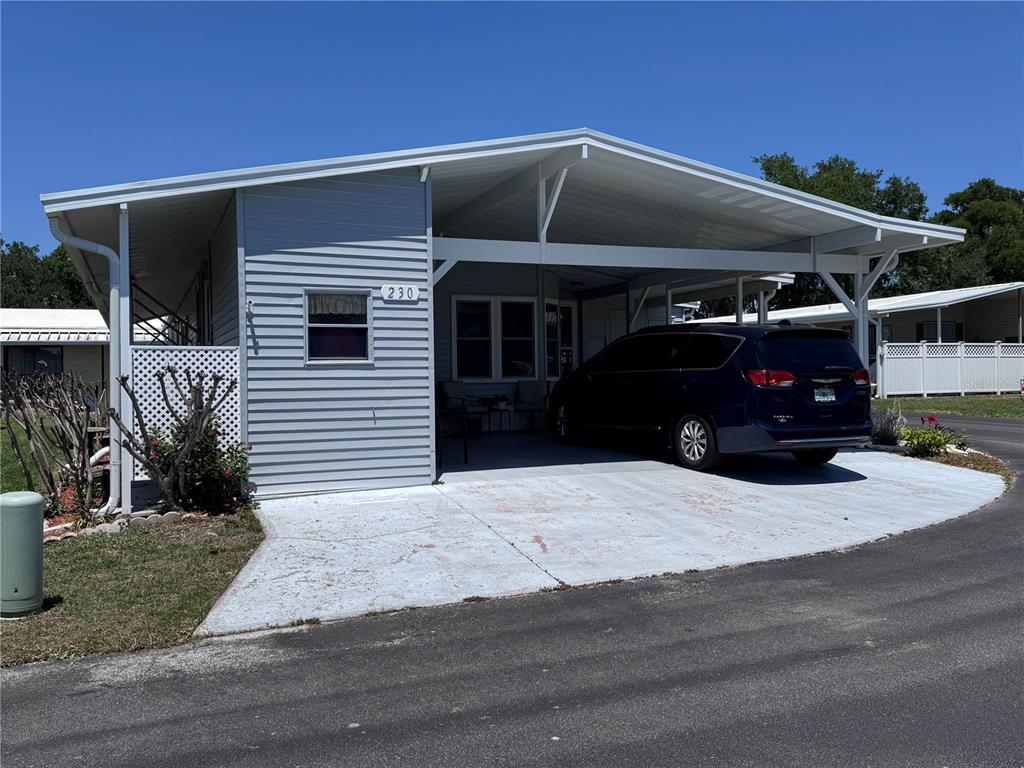 A light gray manufactured home features a large attached carport and a concrete driveway — 2055 S FLORAL AVENUE UNIT 230, BARTOW, FL