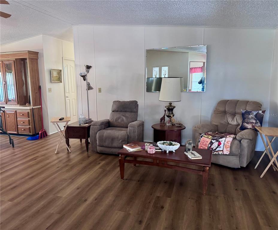 A living room features wood-look flooring, two recliner chairs, a coffee table, and a wall mirror — 2055 S FLORAL AVENUE UNIT 230, BARTOW, FL