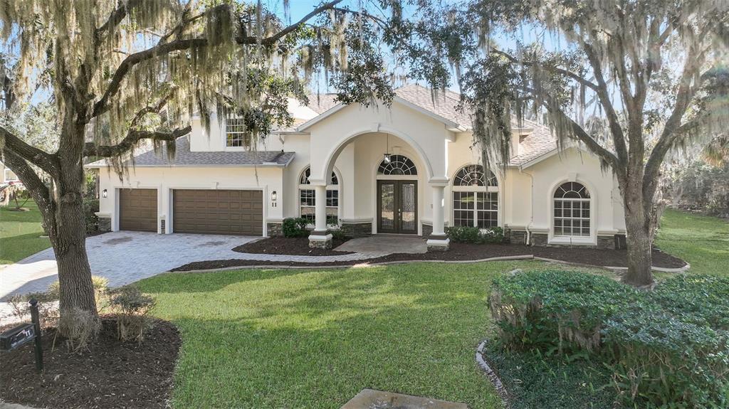 A single-story house with a beige stucco exterior, arched entryway, and a three-car garage — 11 CYPRESS HOLLOW LANE, ORMOND BEACH, FL