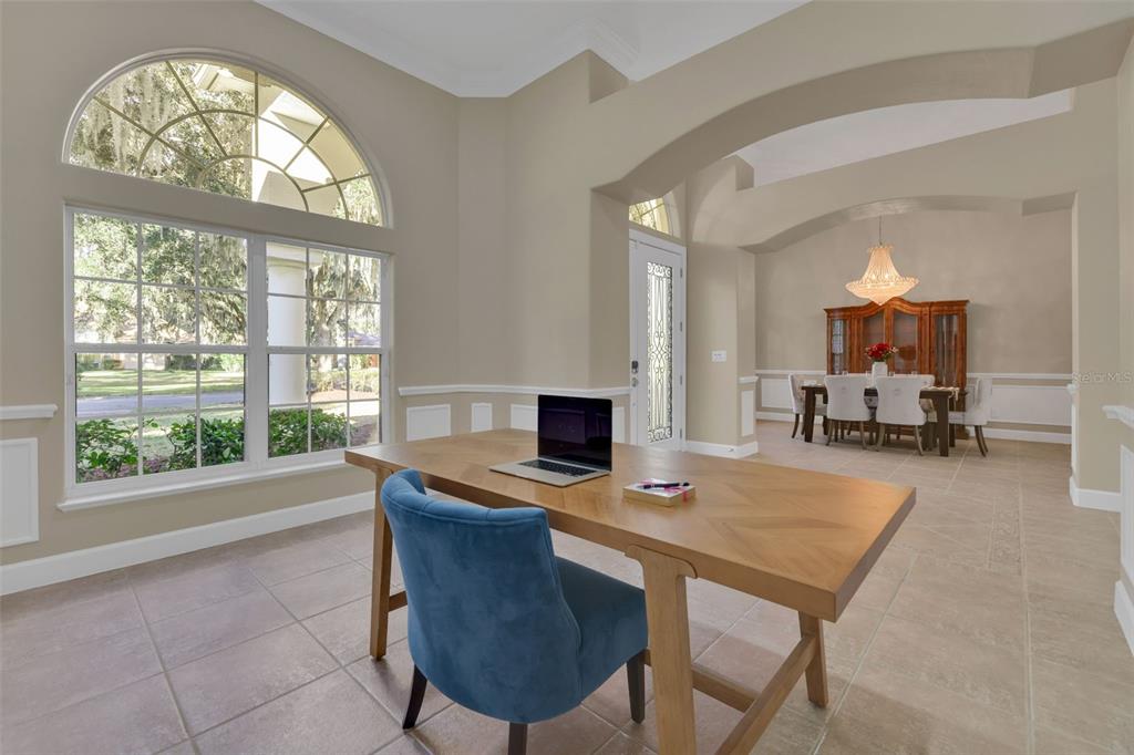 A home office with a wooden desk and blue chair overlooks a formal dining room — 11 CYPRESS HOLLOW LANE, ORMOND BEACH, FL