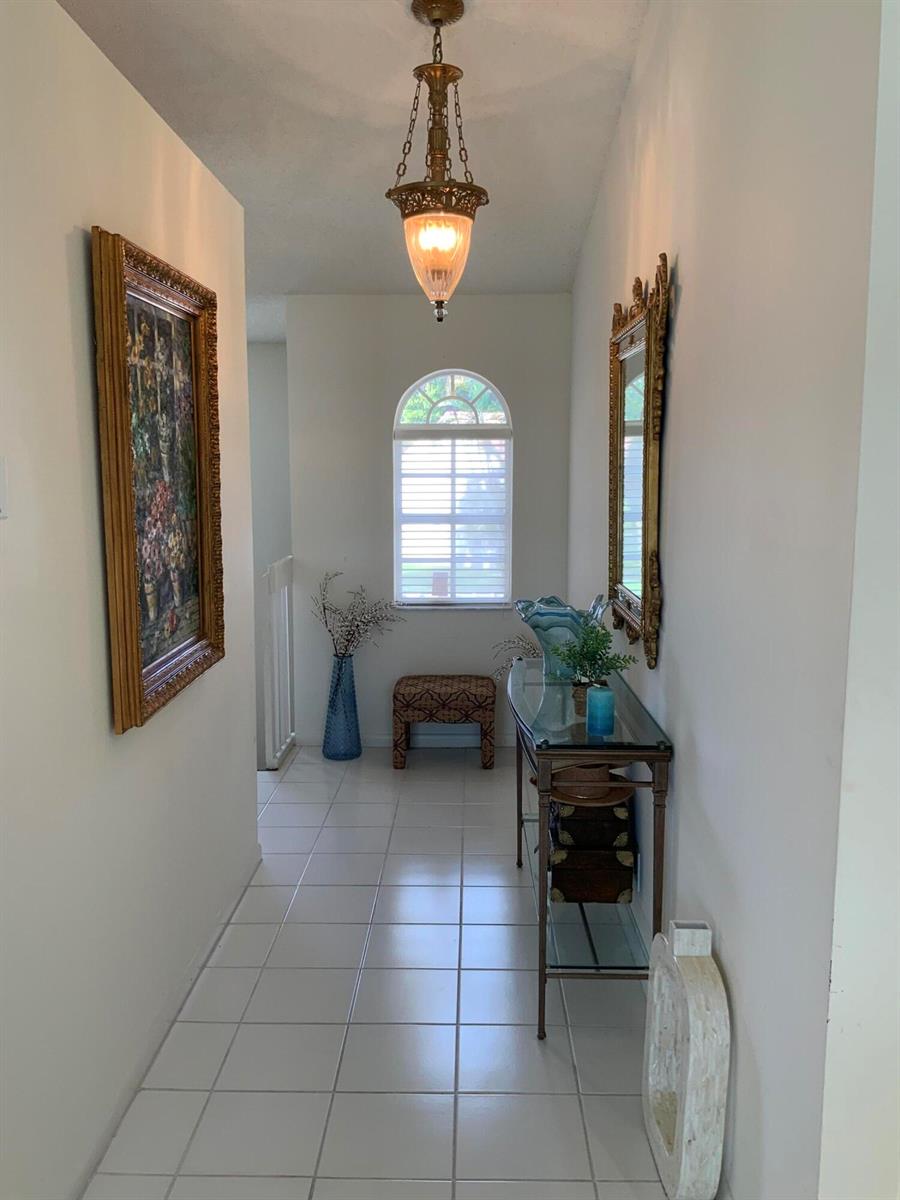 A bright hallway features white tile floors, a glass console table, and a hanging pendant light — 14356 Emerald Lake Drive # 3, Delray Beach FL 33446, DELRAY BEACH, FL