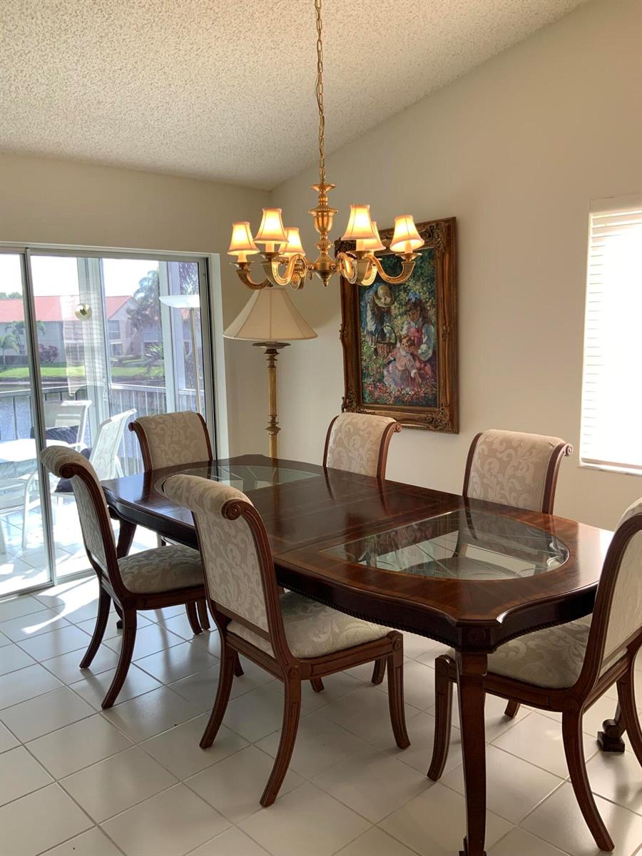 A dining room features a dark wood table with glass inserts, upholstered chairs, and a chandelier — 14356 Emerald Lake Drive # 3, Delray Beach FL 33446, DELRAY BEACH, FL