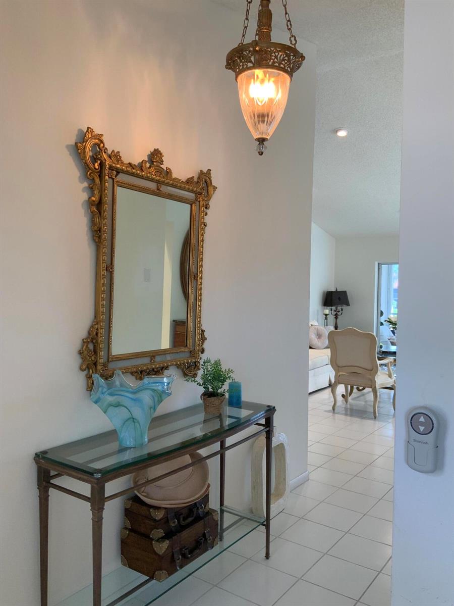 A hallway features a glass console table, an ornate gold mirror, and a hanging pendant light — 14356 Emerald Lake Drive # 3, Delray Beach FL 33446, DELRAY BEACH, FL