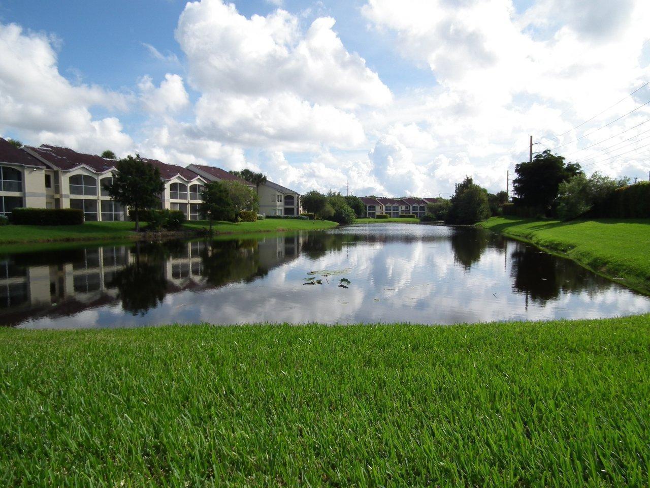 A pond sits in front of apartment buildings under a cloudy blue sky — 815 W Boynton Beach Boulevard # 204, Boynton Beach FL 33426, BOYNTON BEACH, FL