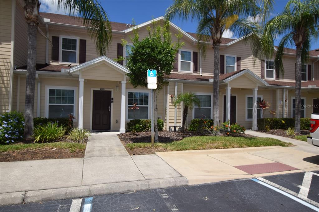 A two-story townhouse exterior with beige siding, a front walkway, and a handicap parking space — 3222 WISH AVENUE, KISSIMMEE, FL