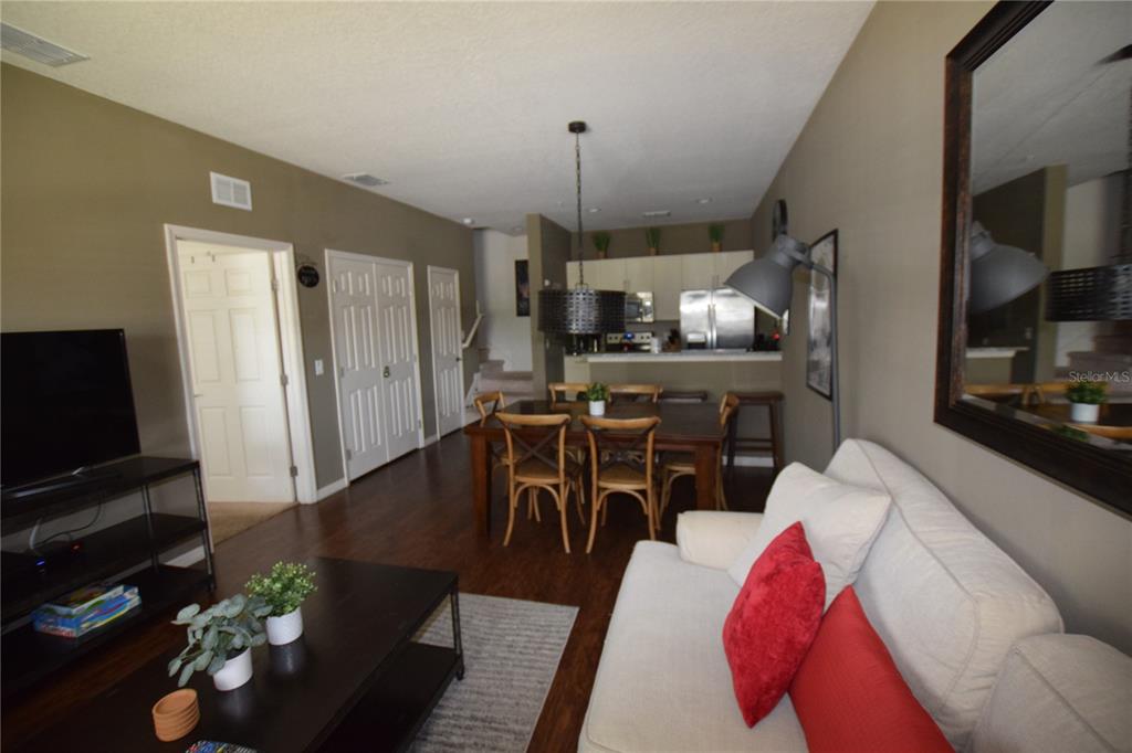 A living room and dining area feature dark wood floors, a sofa, and an open kitchen — 3222 WISH AVENUE, KISSIMMEE, FL