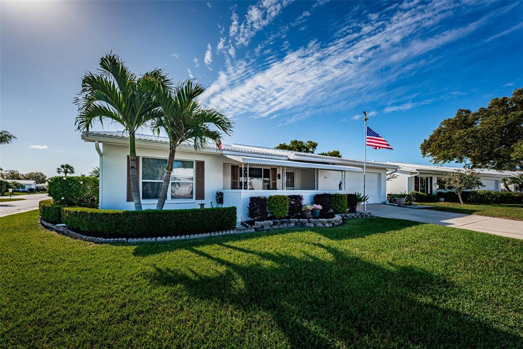 A white single-story house with a palm tree, manicured hedges, and an American flag — 9175 42ND STREET N, PINELLAS PARK, FL