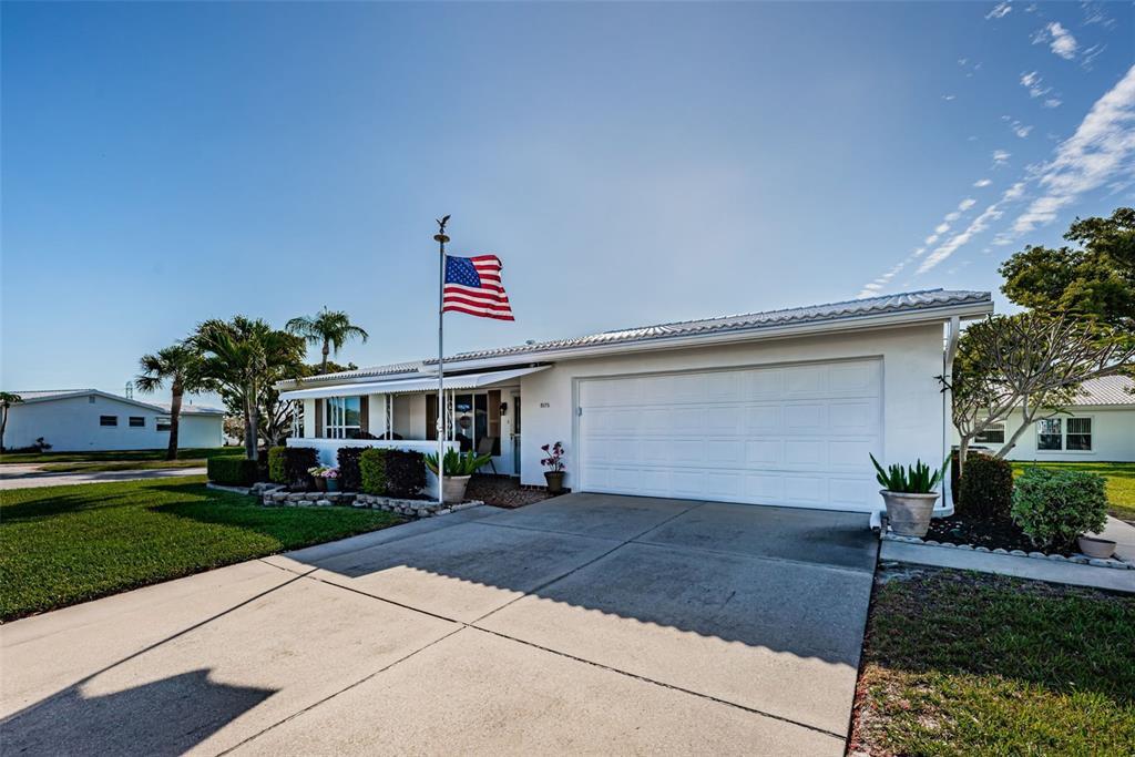 A single-story white house with a two-car garage and an American flag in front — 9175 42ND STREET N, PINELLAS PARK, FL