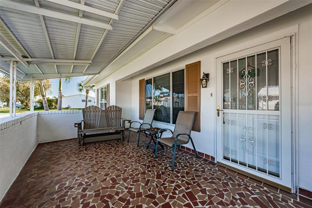 A covered porch features a mosaic tile floor, outdoor seating, and a white storm door — 9175 42ND STREET N, PINELLAS PARK, FL