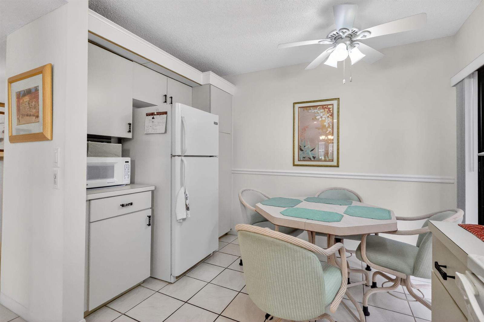 A kitchen dining area features white cabinets, a refrigerator, a ceiling fan, and a table — 10215 N Circle Lake Drive # 101, Boynton Beach FL 33437, BOYNTON BEACH, FL