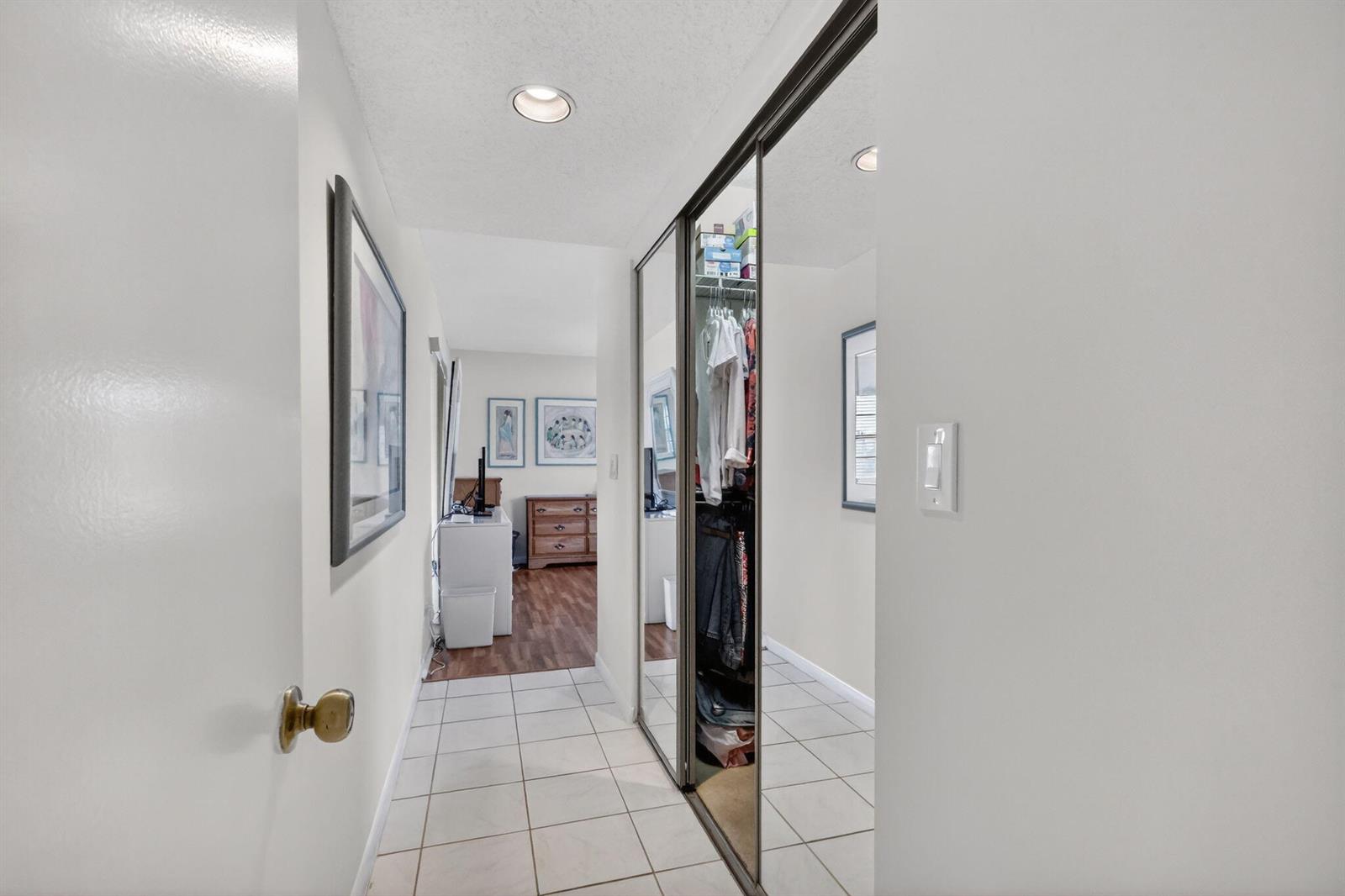 A hallway with tiled flooring leads to a bedroom, featuring a mirrored sliding closet door — 10215 N Circle Lake Drive # 101, Boynton Beach FL 33437, BOYNTON BEACH, FL