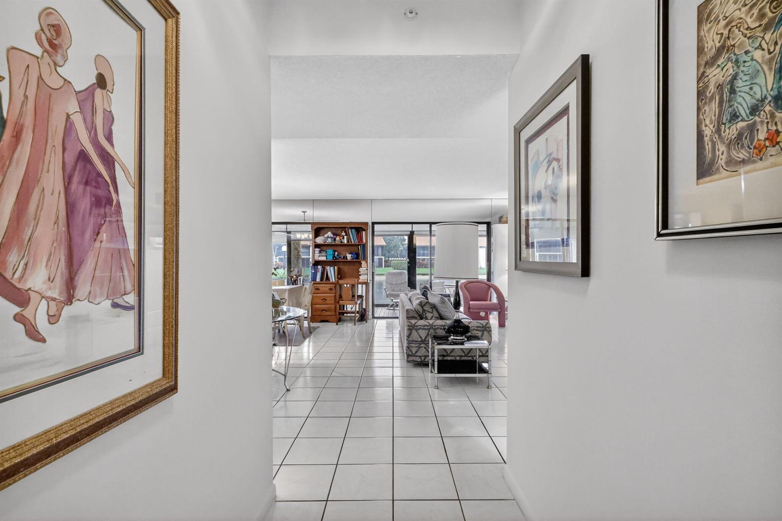 A white-tiled hallway leads into a living area with a sofa, bookshelf, and sliding doors — 10215 N Circle Lake Drive # 101, Boynton Beach FL 33437, BOYNTON BEACH, FL