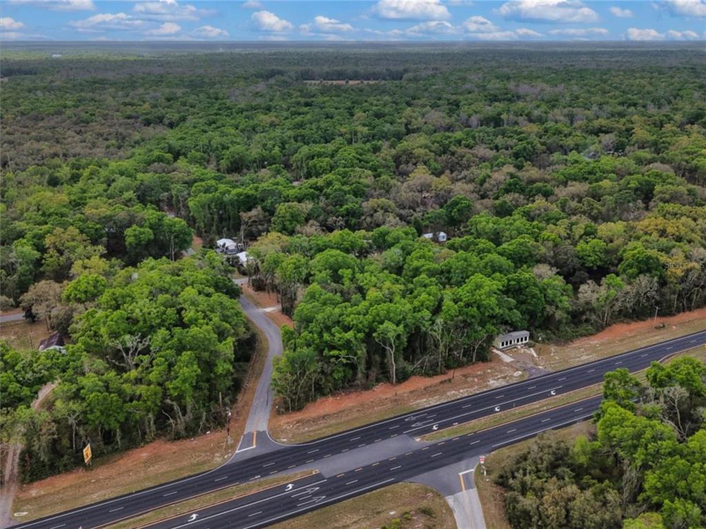 An aerial view shows a paved road intersecting a highway near a wooded residential area — 000 NW US HWY 19, FANNING SPRINGS, FL