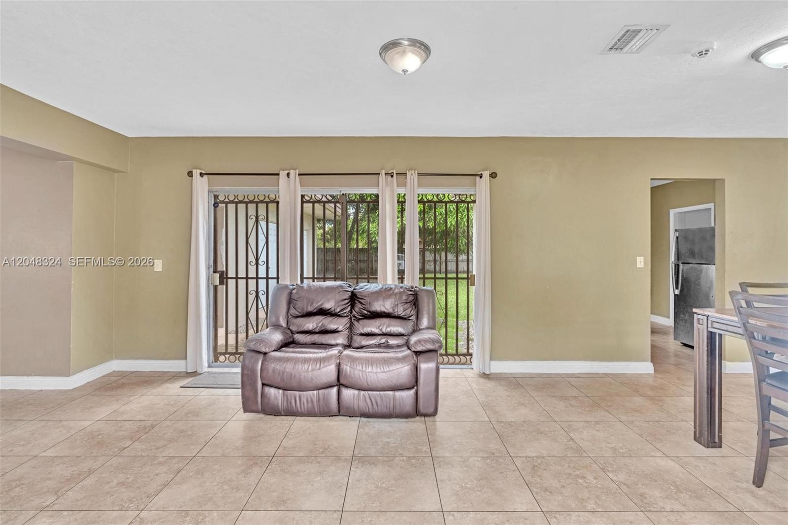 A living room features beige walls, tile flooring, a brown loveseat, and sliding glass doors — 331 NE 176th St, North Miami Beach FL 33162, NORTH MIAMI BEACH, FL