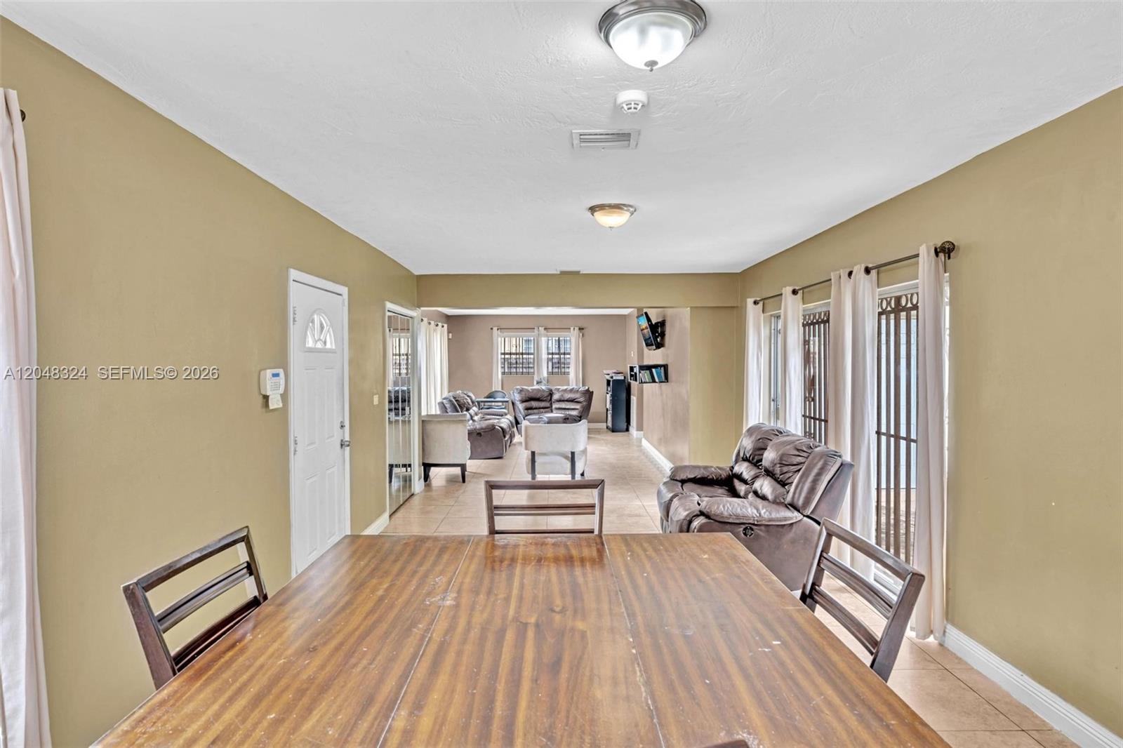 A dining area with a wooden table leads into a living room with tiled floors — 331 NE 176th St, North Miami Beach FL 33162, NORTH MIAMI BEACH, FL