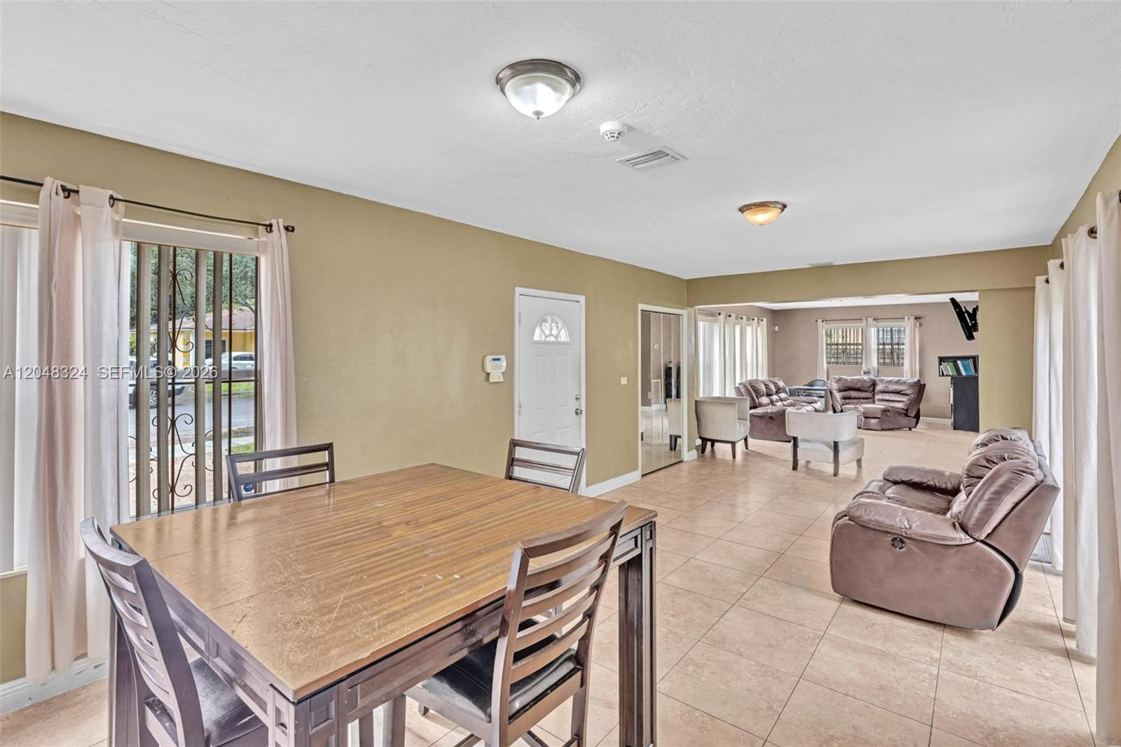 A dining area with a wooden table leads into an open living room with tile floors — 331 NE 176th St, North Miami Beach FL 33162, NORTH MIAMI BEACH, FL