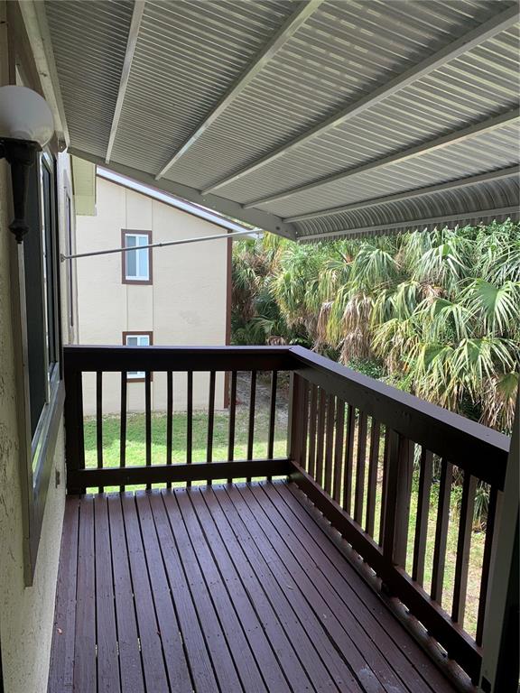 A covered wooden balcony overlooks a grassy yard and palm trees next to a building — 22481 WESTCHESTER BOULEVARD UNIT B31, PUNTA GORDA, FL