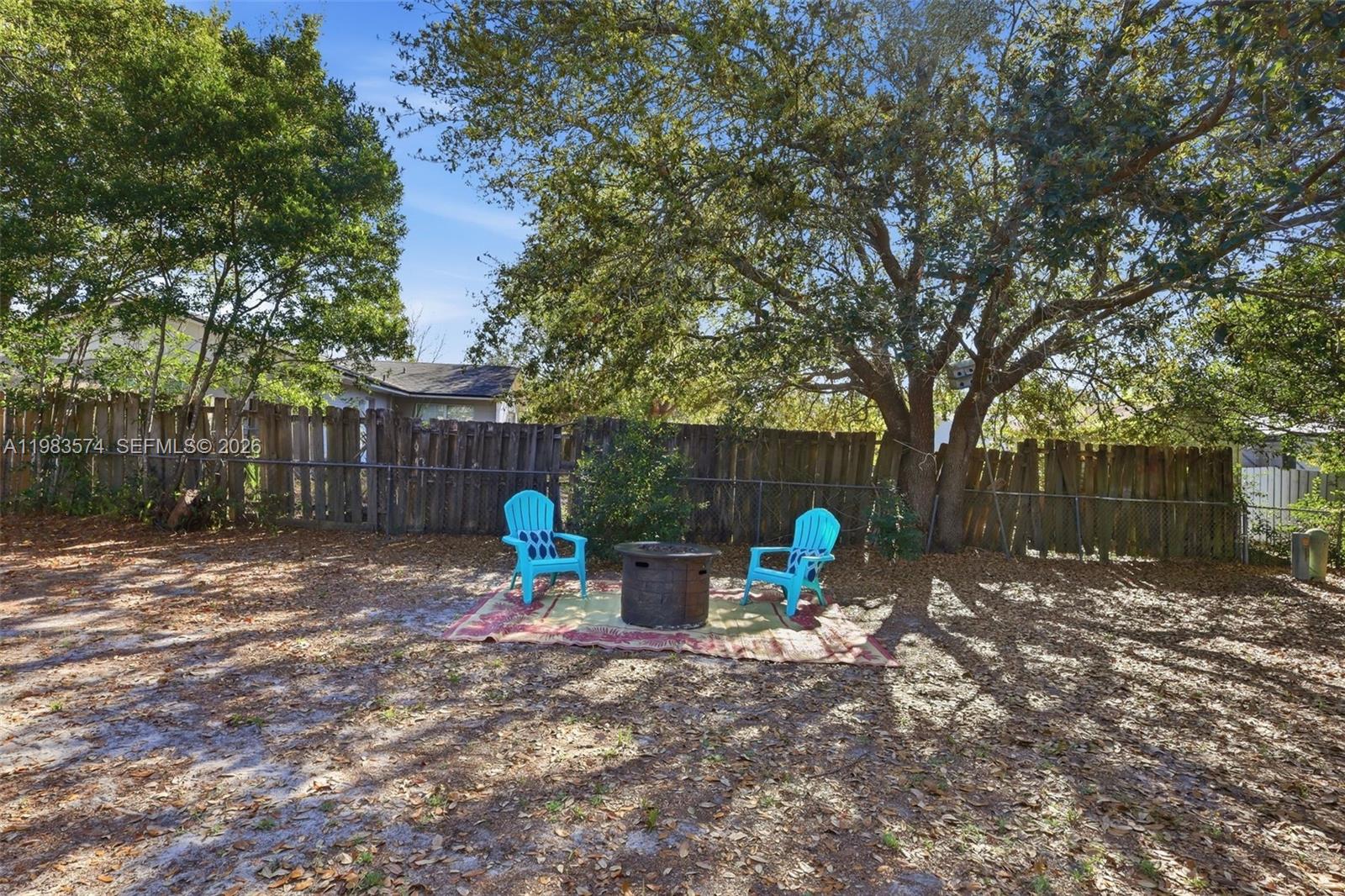 A backyard features a fire pit and two blue chairs on a rug under trees — 2489 ADAMS AVE, Deltona FL 32738, DELTONA, FL