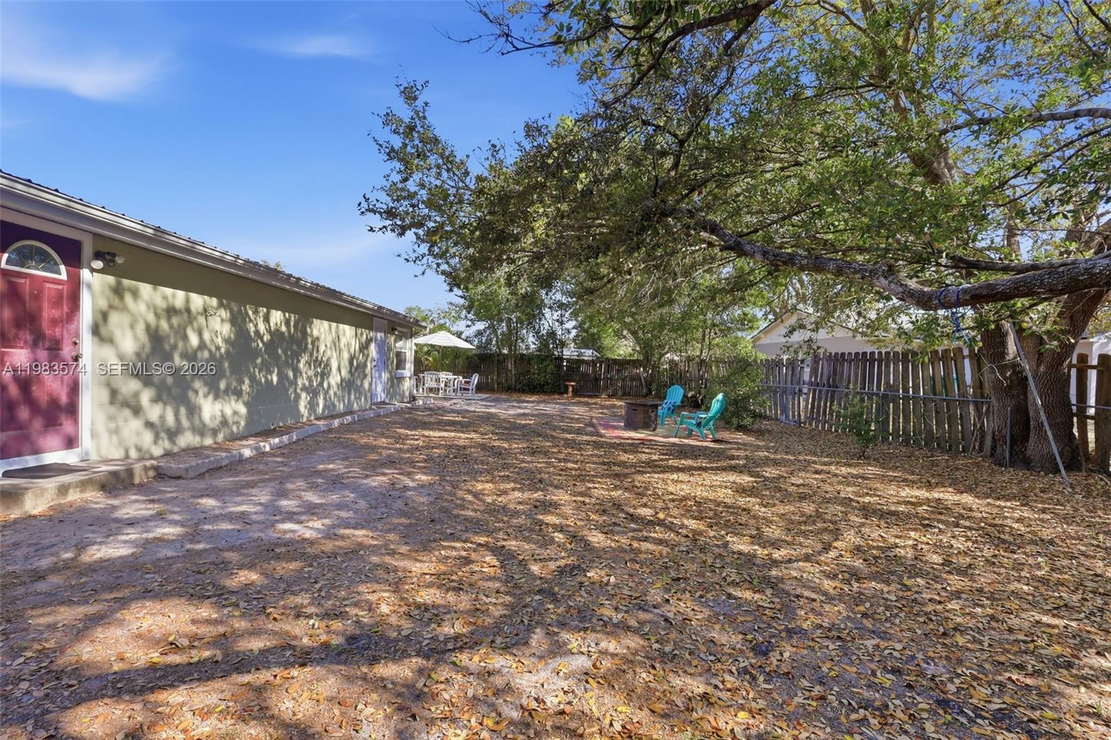 A backyard features a dirt ground covered in leaves, a large tree, and patio furniture — 2489 ADAMS AVE, Deltona FL 32738, DELTONA, FL