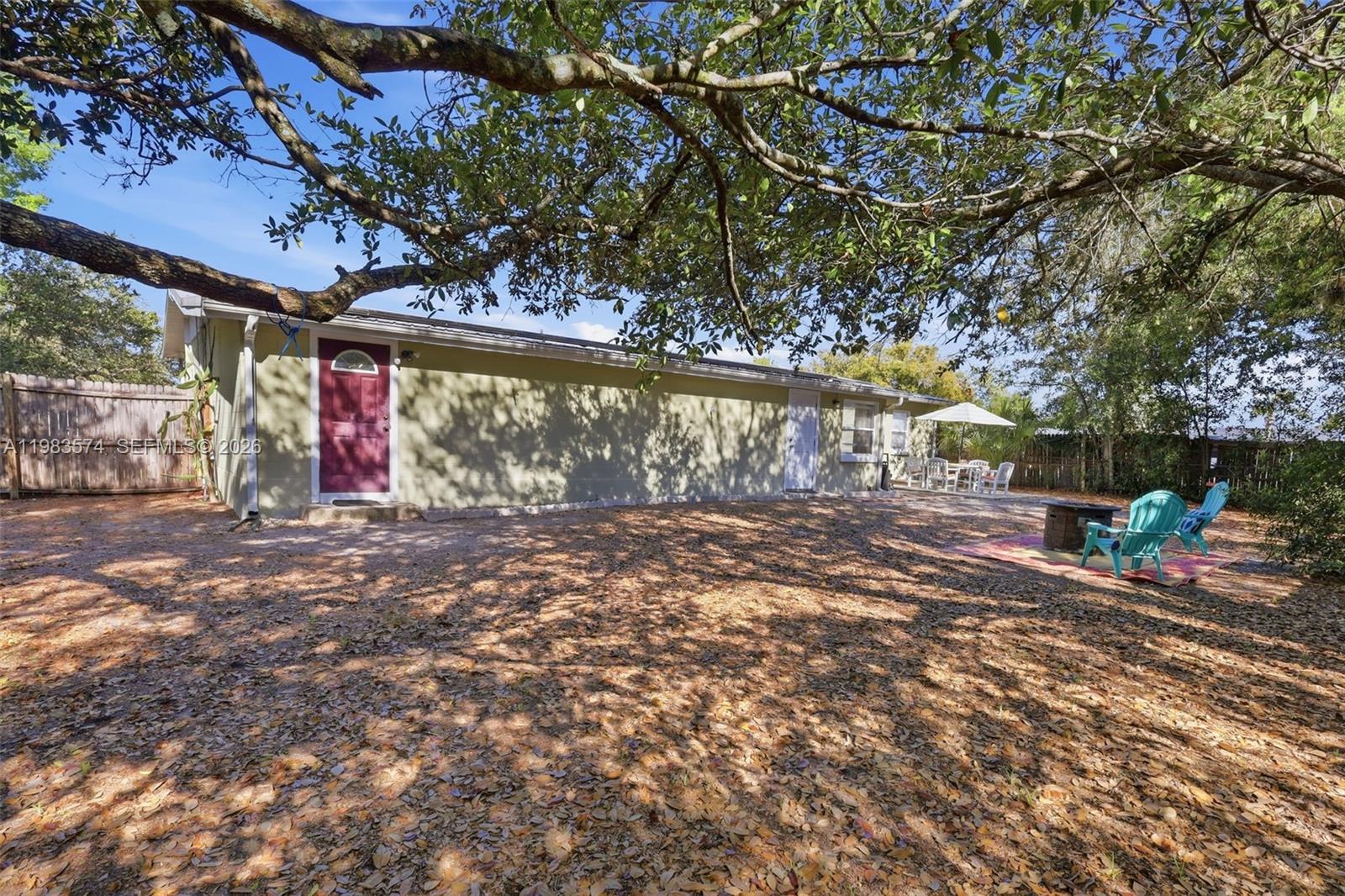 A backyard features a light green house, a large tree, and a patio with chairs — 2489 ADAMS AVE, Deltona FL 32738, DELTONA, FL