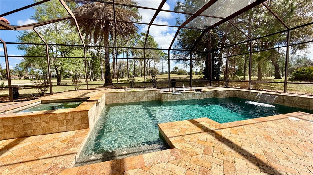 A screened-in pool and spa area with stone tile decking and a golf course view — 6717 SW 179TH AVENUE ROAD, DUNNELLON, FL