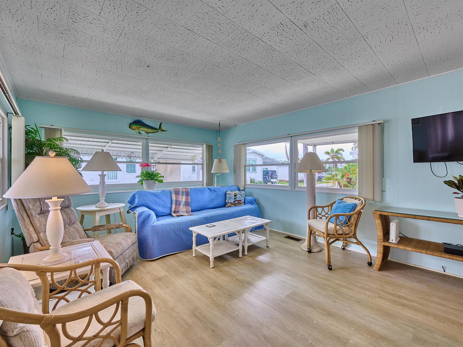 A living room with light blue walls, a blue sofa, wicker furniture, and wood-look flooring — 4300 SE Saint Lucie Boulevard # 123, Stuart FL 34997, STUART, FL