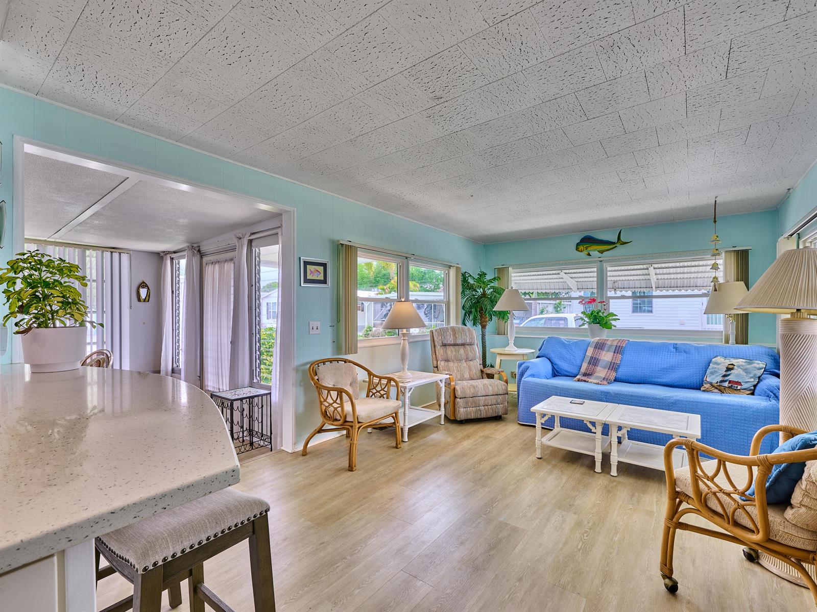 A living room with light blue walls, wood-look flooring, a blue sofa, and rattan furniture — 4300 SE Saint Lucie Boulevard # 123, Stuart FL 34997, STUART, FL