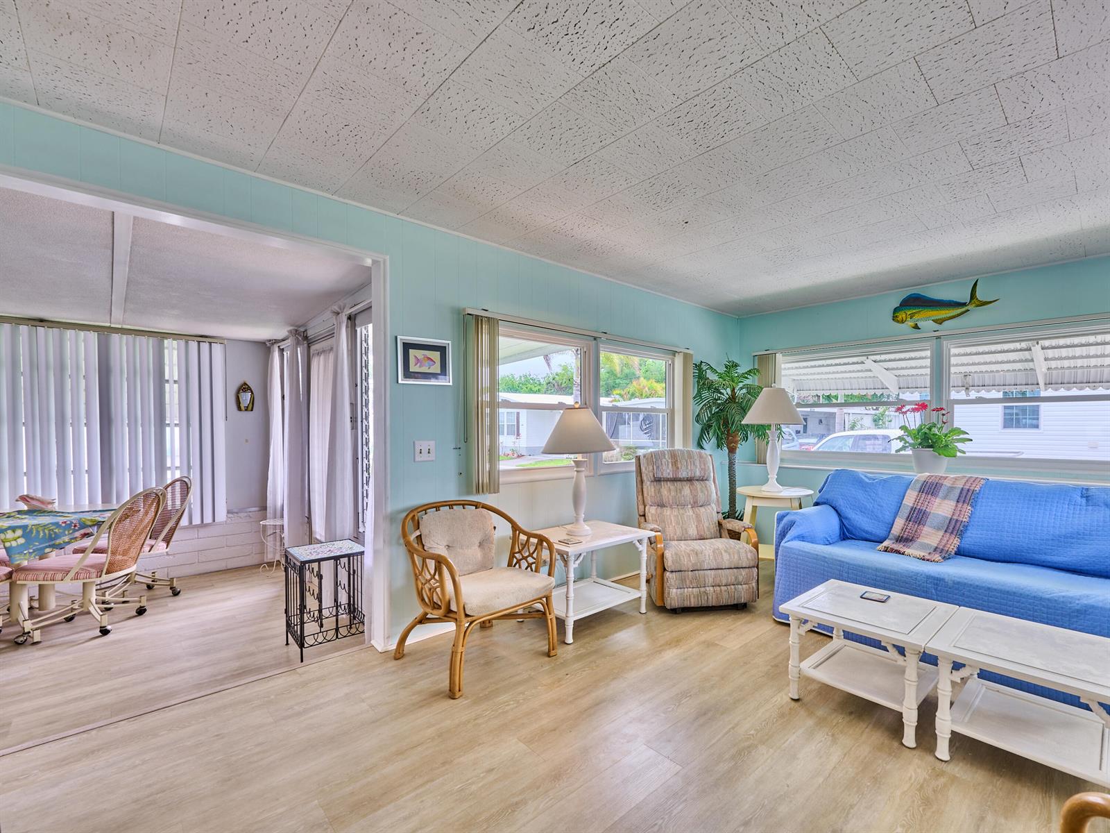 A living room with light blue walls, wood-look flooring, a blue sofa, and wicker furniture — 4300 SE Saint Lucie Boulevard # 123, Stuart FL 34997, STUART, FL