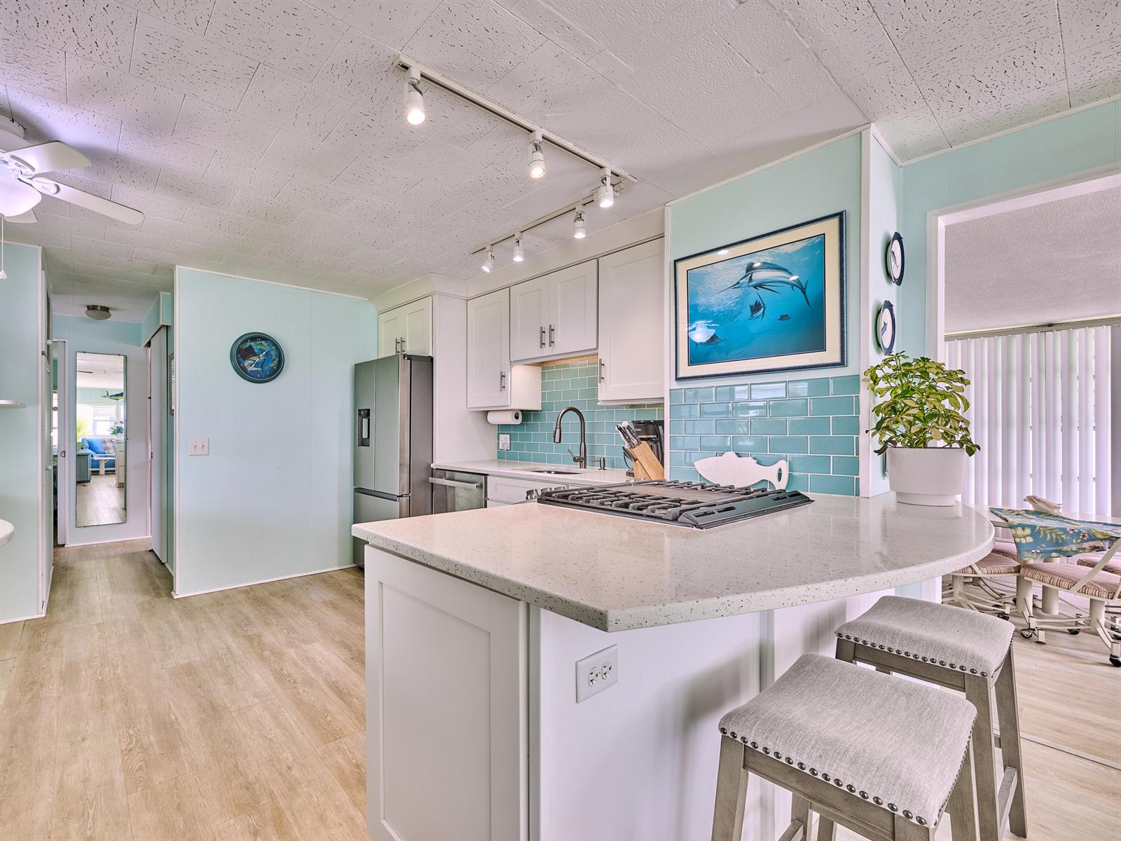 A kitchen features a light-colored island with a gas cooktop, teal backsplash, and white cabinetry — 4300 SE Saint Lucie Boulevard # 123, Stuart FL 34997, STUART, FL