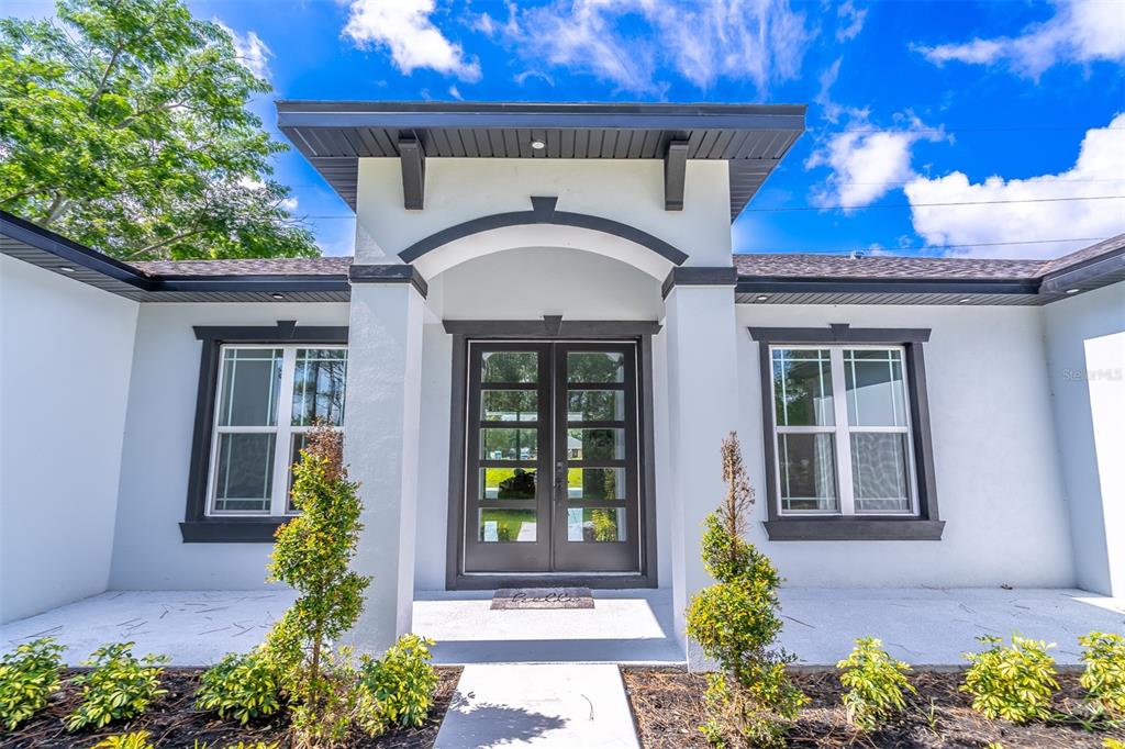The exterior of a modern home features a white facade, dark trim, and double glass doors — 2943 DECKER AVENUE, ORLANDO, FL
