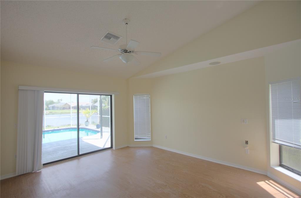 An empty living room with vaulted ceilings, light wood flooring, and sliding doors to a pool — 6907 RANCH ROAD, SARASOTA, FL