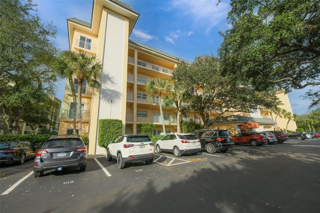 A multi-story apartment building with balconies stands behind a parking lot filled with cars — 8630 MIDNIGHT PASS ROAD UNIT 502A, SARASOTA, FL