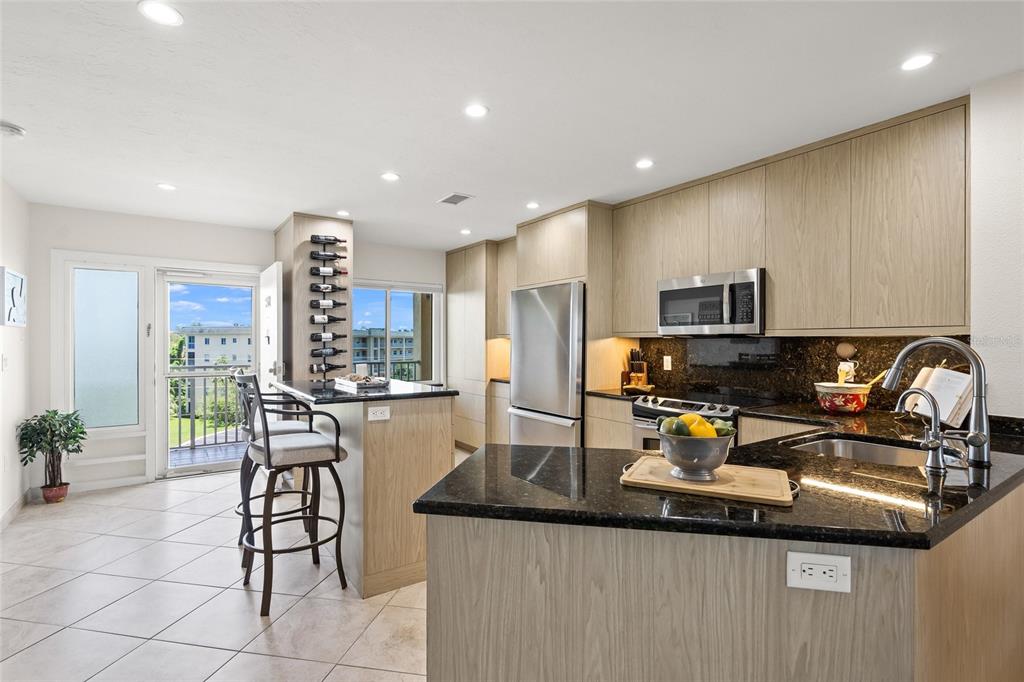 A kitchen features light wood cabinets, dark granite countertops, stainless steel appliances, and a balcony — 8630 MIDNIGHT PASS ROAD UNIT 502A, SARASOTA, FL