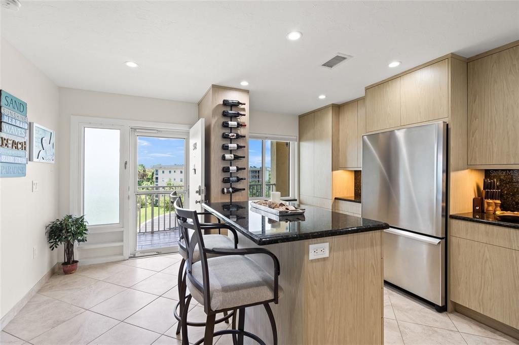 A kitchen features a granite-topped island, light wood cabinets, stainless steel appliances, and balcony access — 8630 MIDNIGHT PASS ROAD UNIT 502A, SARASOTA, FL