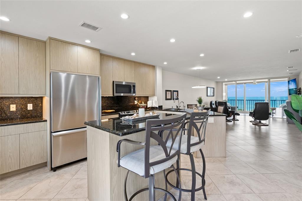 A modern kitchen with light wood cabinets and a dark granite island overlooks the ocean — 8630 MIDNIGHT PASS ROAD UNIT 502A, SARASOTA, FL