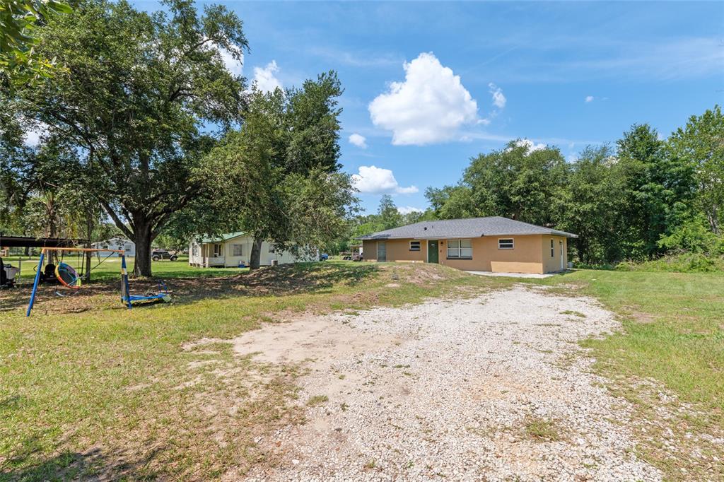 A tan, single-story house sits on a gravel driveway next to a grassy yard — 17611 FL33, GROVELAND, FL